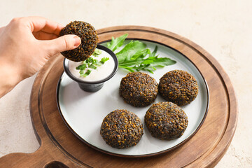 Female hand with tasty falafel balls and sauce on light background