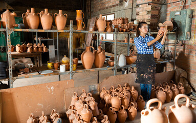 Young woman potter putting in order crafts in pottery studio
