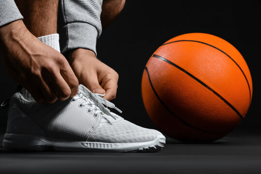 Male basketball player tying shoelaces on dark background, closeup