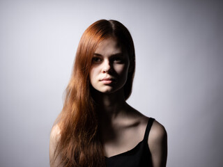 Naklejka premium Beautiful woman with red hair in a black dress on a gray background bared shoulders