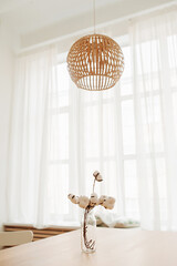 stylish decor minimalist boho style. bouquet natural cotton inglass vase on table next to huge window with white curtains and bamboo eco chandelier. ready-to-print interior poster, selective focus