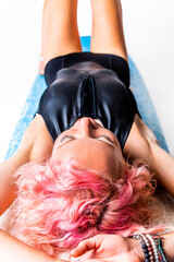 A very fit female with blonde and pink hair in a black bathing suit is lying on a blue surfboard