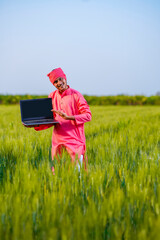 Young indian farmer showing laptop screen at wheat field