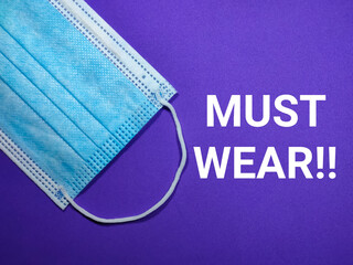 Selective focus.Word MUST WEAR with face mask on purple background.Shot were noise and film grain.