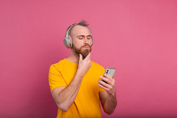 Handsome man in casual listening to music with headphones isolated on pink background