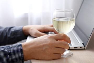Man with glass of white wine working at laptop. Remote work at home or relax at office