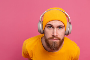 Handsome man in casual listening to music with headphones isolated on pink background