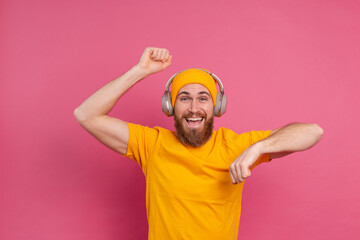 Fototapeta premium Handsome man in casual dancing with headphones isolated on pink background