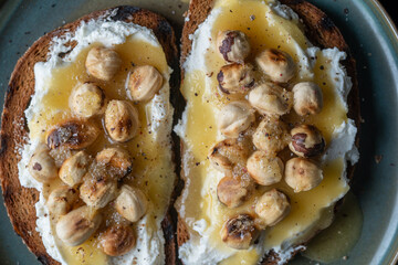 Two bread toast with cream cheese, roasted hazelnuts, honey, pepper and salt, close up, top view