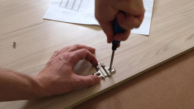 Installation of furniture accessories with hands and a screwdriver on furniture.
