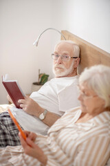 Fototapeta premium Aged married couple lying in bed and reading and feeling good