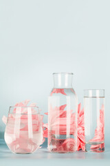 pink flowers distorted through water in glasses and bottle on blue background. Home decor, eco friendly, relax, gardening concept. copy space