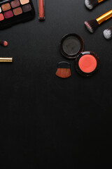 Overhead shot of feminine desk with with lipsticks, eye palette, face powder, brushes and copy space on dark background.