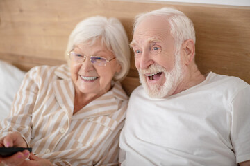 Grey-haired woman switching on tv and smiling nicely