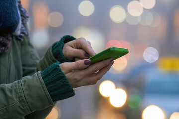 Woman using modern smartphone on the street with defocused city lights in the background.