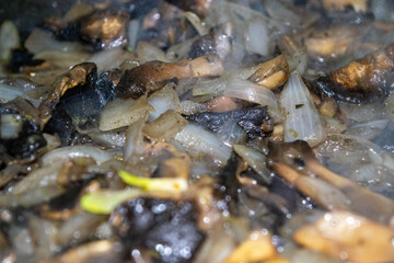 Wild mushrooms with onions are fried in a frying pan.