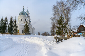 Rural winter landscape with a majestic white church towering over the ancient Ural village of...