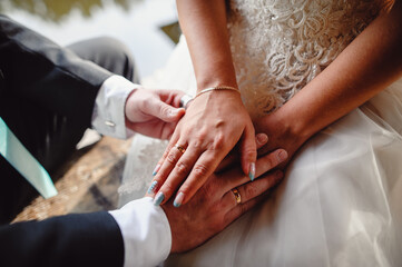 Obraz na płótnie Canvas Bride in white wedding dress and groom in black tuxedo holding hands, close up. Gold wedding rings on the fingers of a married couple holding each other's hands. Wedding ceremony