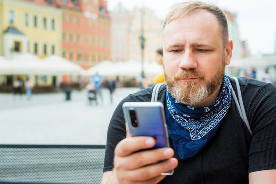 adult man in bandana as a face mask uses smartphone outdoor on city cafe terrace. solo outdoor activities. safety city walk