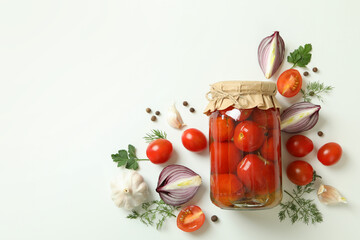 Jar of pickled tomatoes and ingredients on white background
