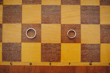 Two wedding rings on a chessboard, close up.  Film noise