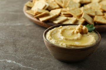 Tray with crackers and bowl of hummus on gray background