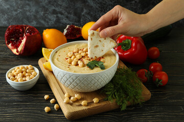 Female hand dips pita in tasty hummus on wooden table
