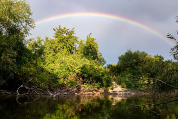 Rainbow over river in green forest. Idyllic landscape