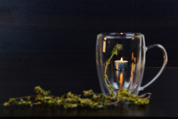 Herbal tea leaves in transparent cup,  black background. Burning candle behind a transparent glass. Tea romantic design background.