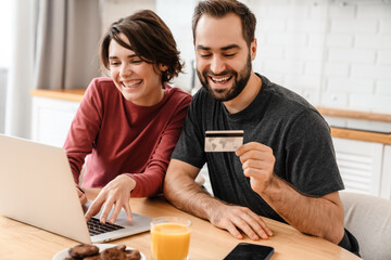 Happy young couple using laptop and credit card while sitting at home