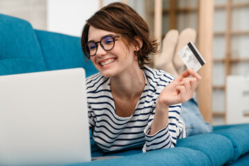 Happy beautiful woman using credit card and laptop on couch