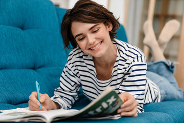 Happy beautiful student girl doing homework while lying on couch