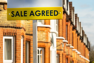 Naklejka premium Estate agent 'Sale Agreed' sign on street of red brick houses 