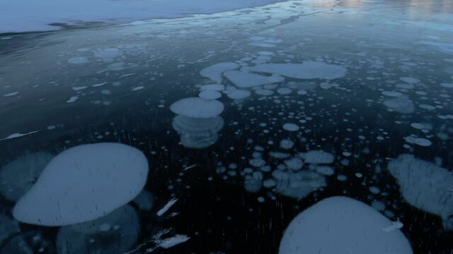 Methane Bubbles Frozen In Surface Of Arctic Circle Lake Ice - Tilt Up. Climate change raises bubbling methane CH4 gas under an Arctic circle lake's solid surface due to permafrost melting.