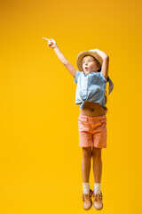 full length of shocked kid in straw hat pointing away with finger on yellow