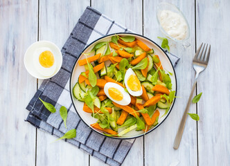 Salad of fried sweet potato or pumpkin, arugula, fresh cucumber and boiled egg on a white plate on a light wooden background. Sweet potato recipes.