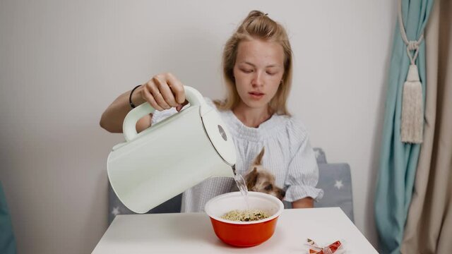 The girl pours boiling water into a plate of instant noodles