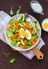 Roasted sweet potato or pumpkin salad, arugula, fresh cucumber and boiled egg on a ceramic plate on a brown concrete background. Sweet potato recipes.