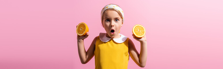 shocked girl in headscarf holding orange halves isolated on pink, banner