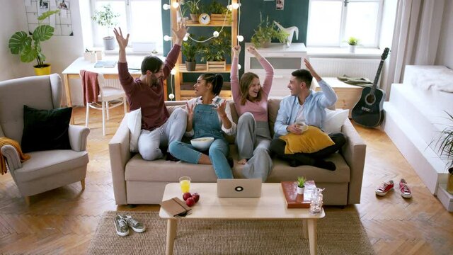 A group of excited flatmates sitting on sofa and watching movie, house sharing concept.