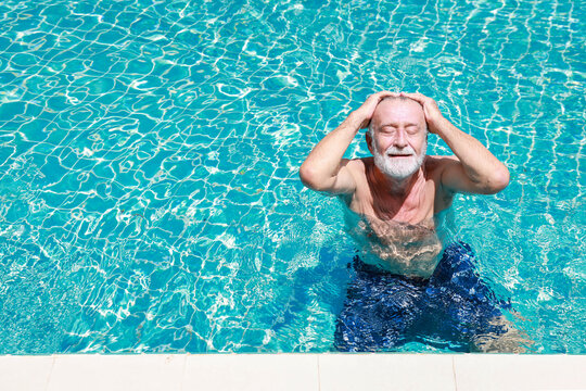 Happy elderly caucasian swimming in pool during retirement holiday with relaxation and smiling. Old man having good time in hotel outdoor with happy face