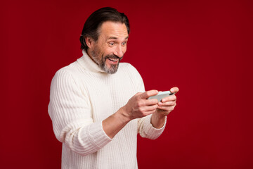 Photo of mature happy positive excited crazy smiling man playing video games on phone isolated on red color background