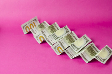 Accordion folded hundred dollar bills on a pink background.