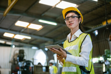 portrait asian woman engineer industry heavy worker wearing hardhat and holding tablet standing at machine area in factory, engineering industrial concept.