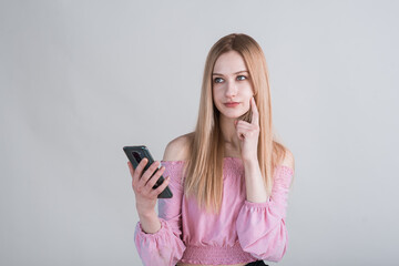 Fototapeta premium Portrait of a pensive blonde girl with a smartphone in the studio on a white background