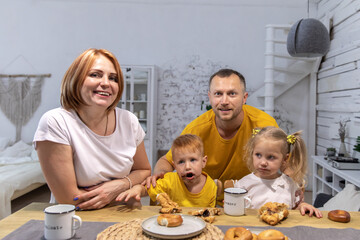 family has breakfast together. parents and children in the kitchen. family eats croissants