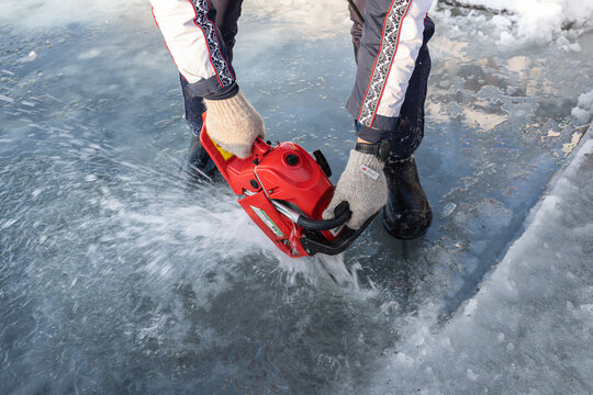 Russia, River Volga Kama - Jan 17th 2020. Man carving an ice hole entry with a motor saw chainsaw for ice scuba diving