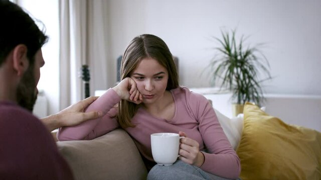 Sad young woman talking to friend on sofa, house sharing concept.