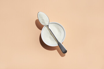 Collagen powder in a silver spoon and white ceramic bowl on peach background.