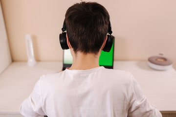 Back view of young boy play game on laptop. Green screen. Steamer in earphones capture video on web camera